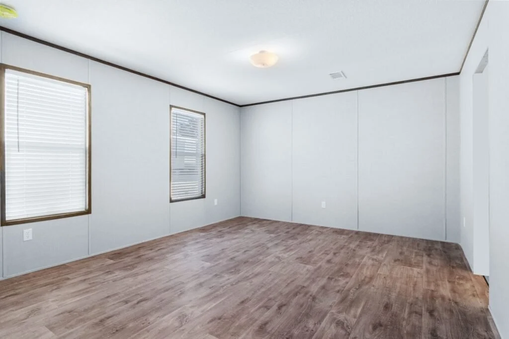 Empty room with white walls, two windows with blinds, wood flooring, and ceiling light fixture.