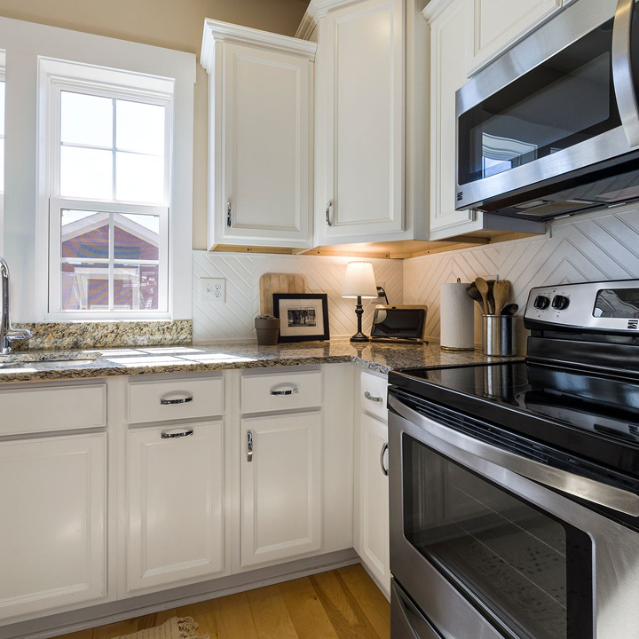 Modern kitchen with white cabinets, granite countertops, stove, microwave, and a window above the sink.