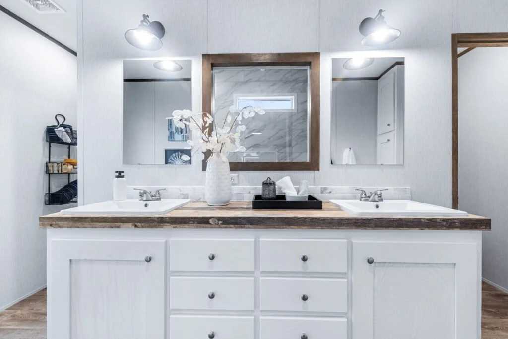 Bathroom vanity with two sinks, mirror, and decorative flowers in a vase, with storage baskets on the side.