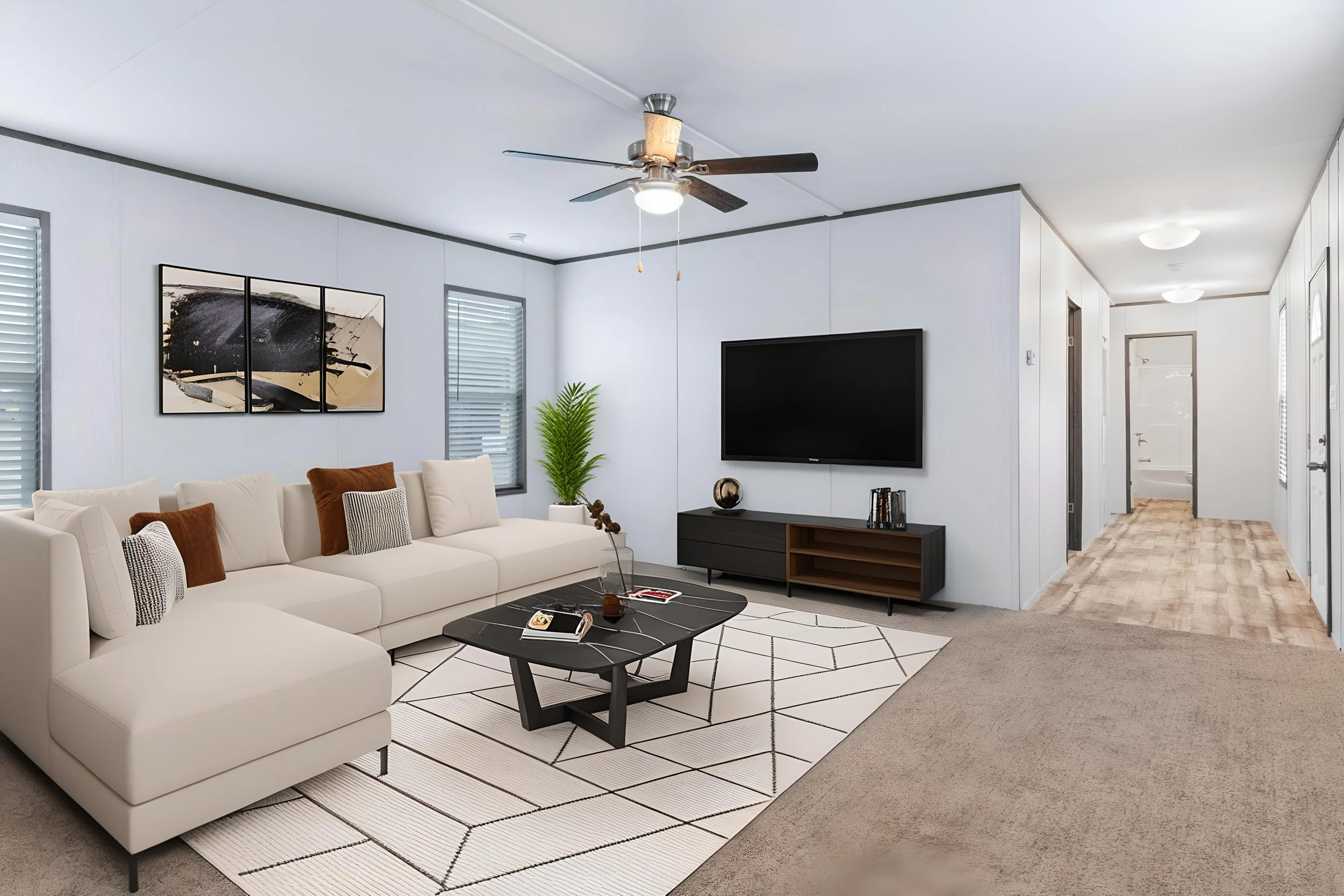 Living room with white sofa, black coffee table, abstract artwork on wall, flat-screen TV, and ceiling fan. There is a hallway in the background with a door at the end.