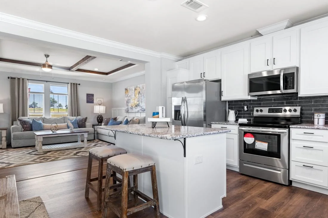 Open-concept living room and kitchen with white cabinets, stainless steel appliances, granite countertops, and hardwood floors.