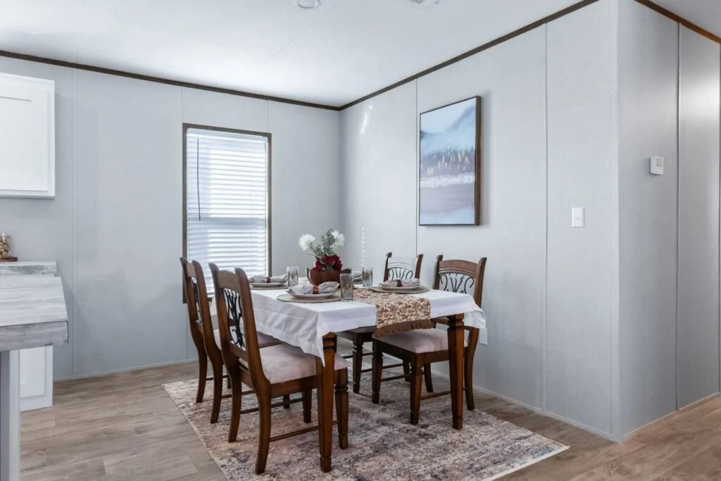 Dining room with a wooden table, six chairs, a white tablecloth, a small table runner, centerpiece, and wall art, with a window and radiator on the wall.