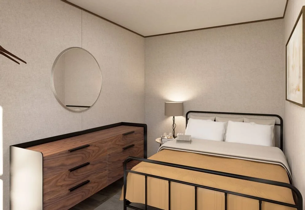 A bedroom with a bed, a wooden dresser, a round mirror, a table lamp, and wall art.