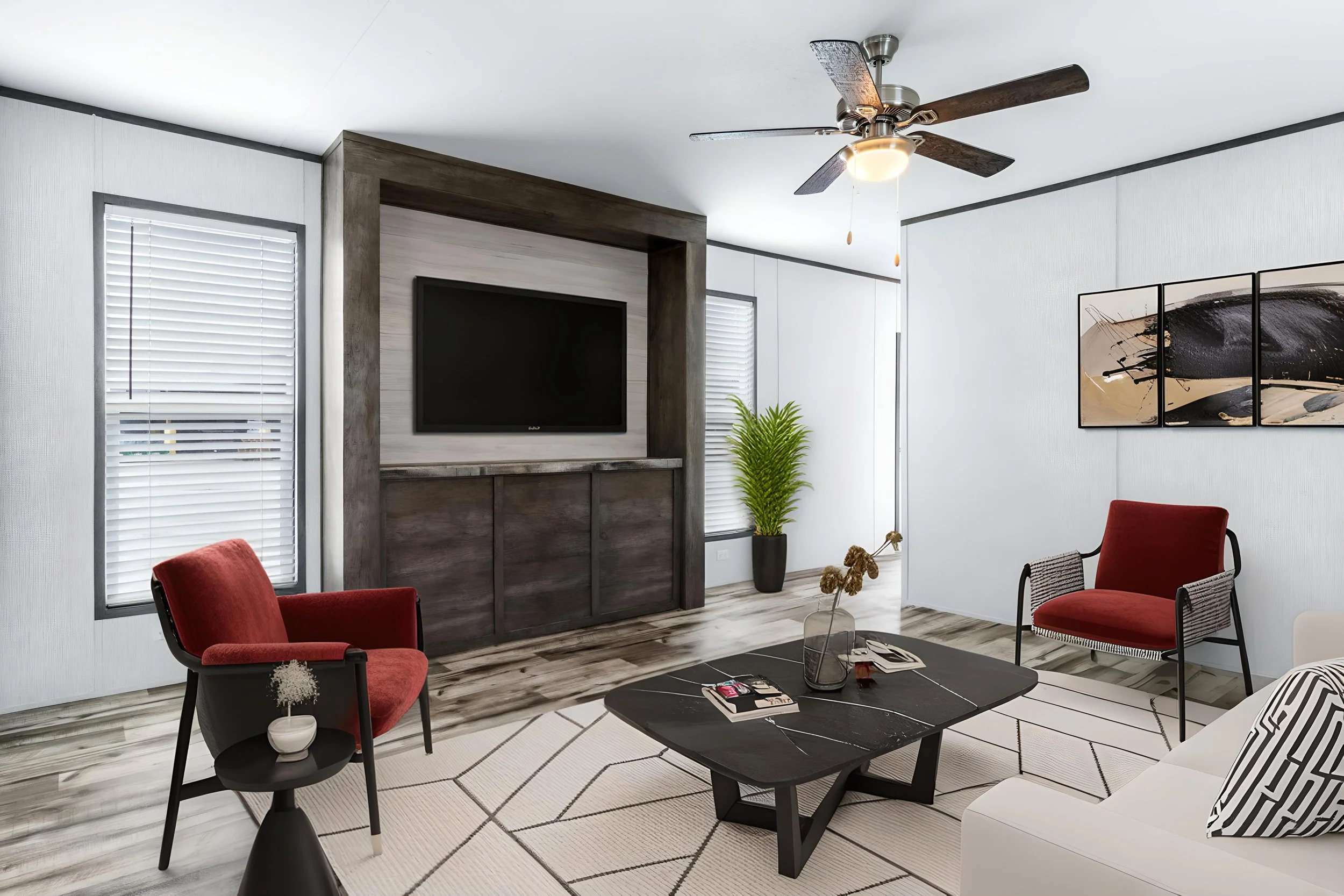 Living room with white walls, a flat-screen TV on a wood-paneled wall, red and white chairs, a black coffee table with magazines, a black and white rug, framed artwork, and plants.