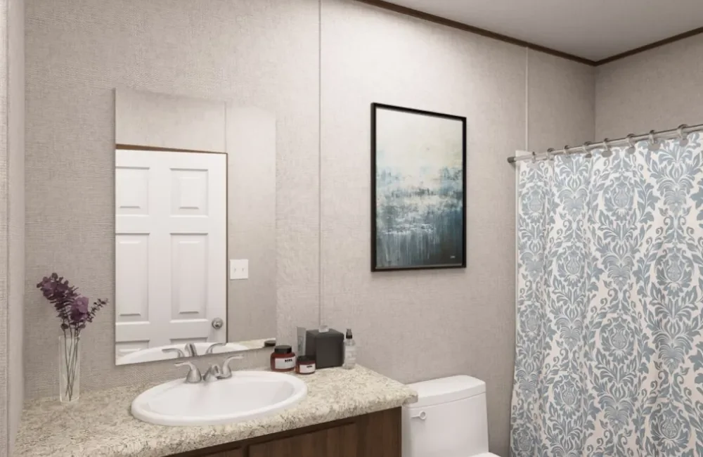 Bathroom with a mirror, a sink with a granite countertop, a small vase with purple flowers, a toilet, a framed abstract painting, and a floral-patterned shower curtain.