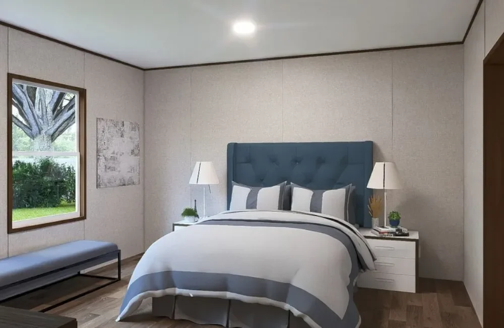 A bedroom with a bed, each with gray and white striped bedding and four pillows, flanked by white nightstands with lamps, a bench by the window, and a view of trees outside.