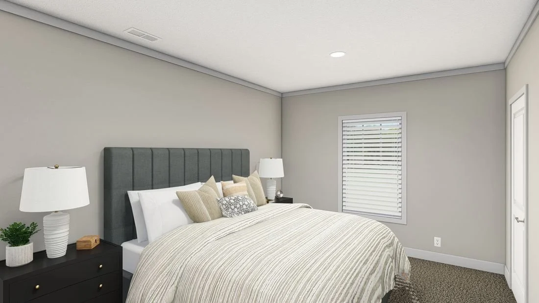 A bedroom with a large bed, dark gray headboard, white bedding, multiple pillows, two nightstands with white lamps, a window with white blinds, and a door.