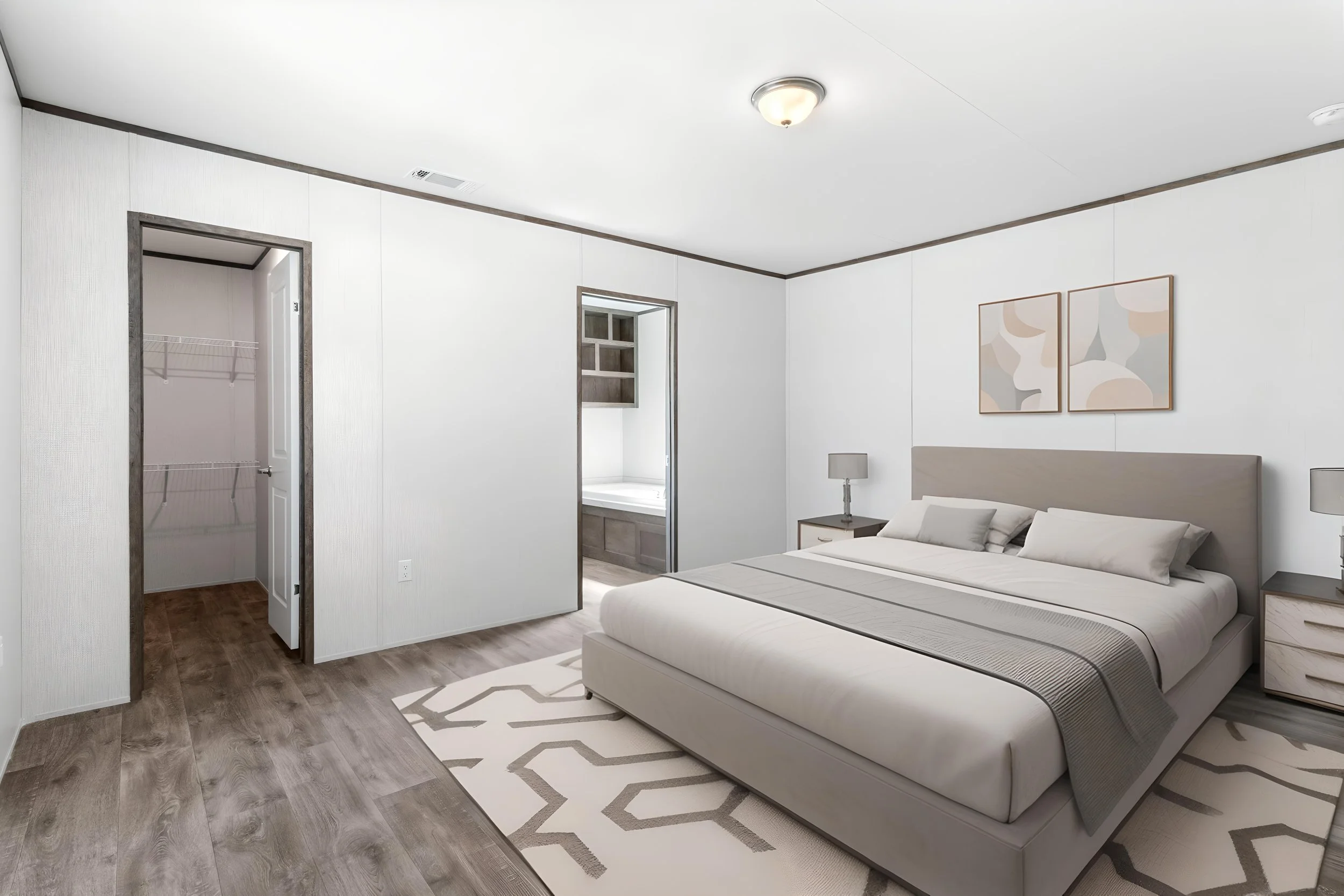 A modern bedroom with a light-colored bed, bedside tables with lamps, abstract wall art, and a patterned area rug on wood flooring. There are two doorways, one leading to a closet and the other to a bathroom with a window.