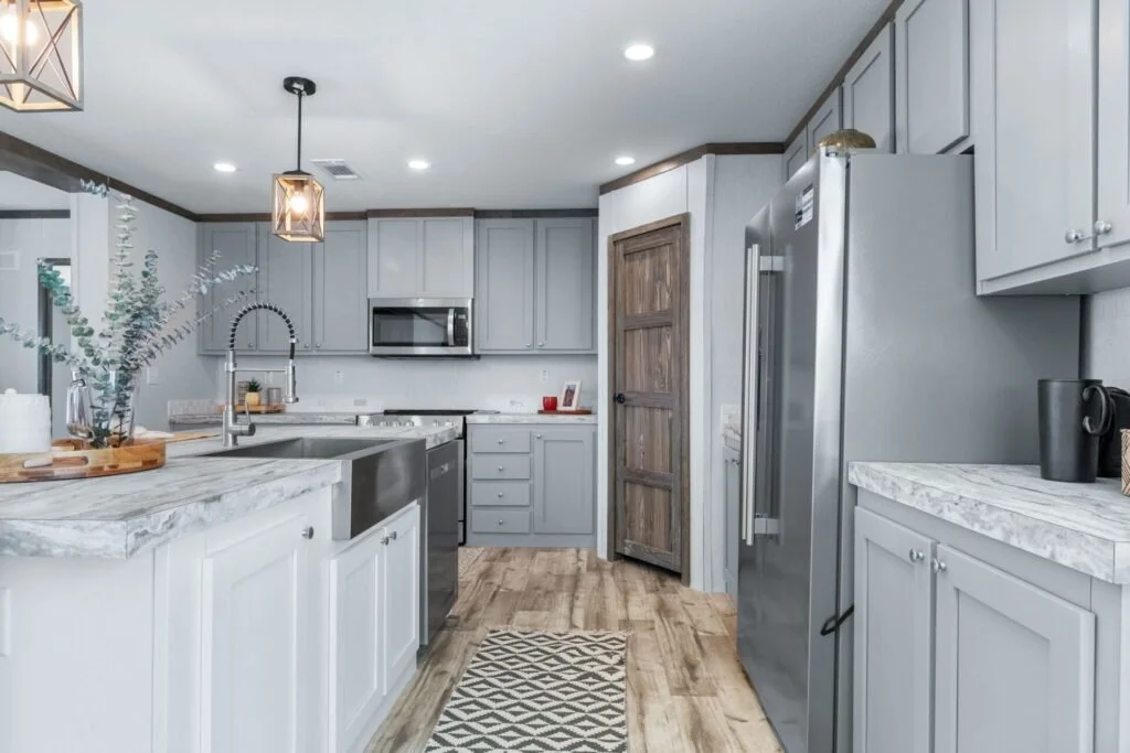Modern kitchen with gray cabinets, stainless steel appliances, marble countertops, and wooden accents including a barn door.