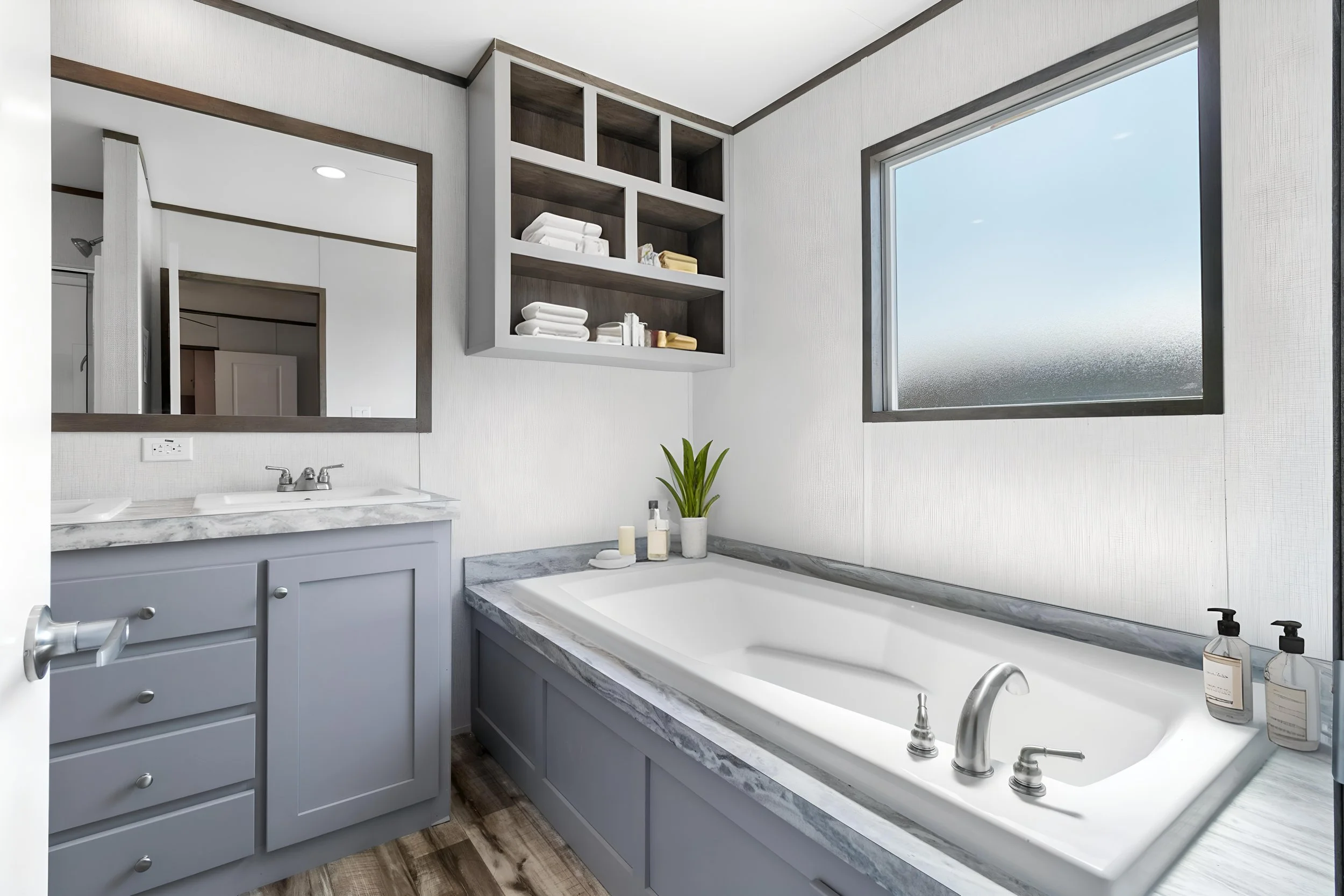 A bathroom with a large bathtub, a mirror, open shelves with towels, and a window, decorated in white and gray tones.
