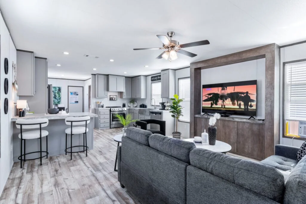 Open-concept living room and kitchen with gray furniture, white cabinetry, a ceiling fan, and a mounted flat-screen TV.