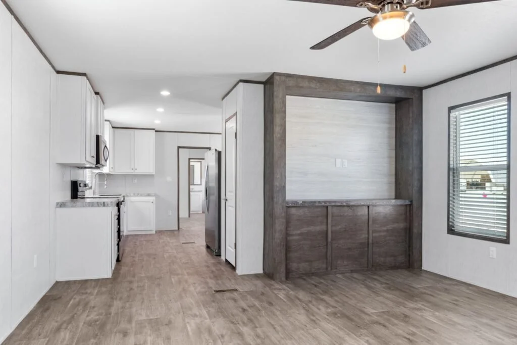 Interior of a modern kitchen and dining area with white cabinets, wood flooring, a ceiling fan, and a large window.