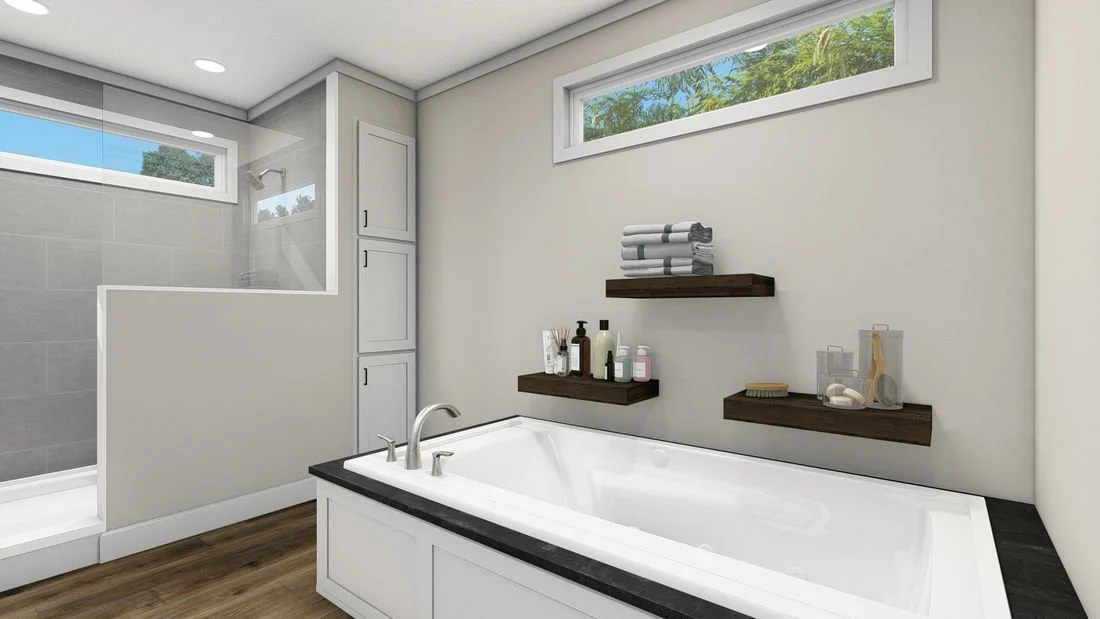 Bathroom with a white bathtub, two floating dark wood shelves with towels and toiletries, a window with green foliage outside, a glass-enclosed shower with tiled walls, and a light-colored cabinet.
