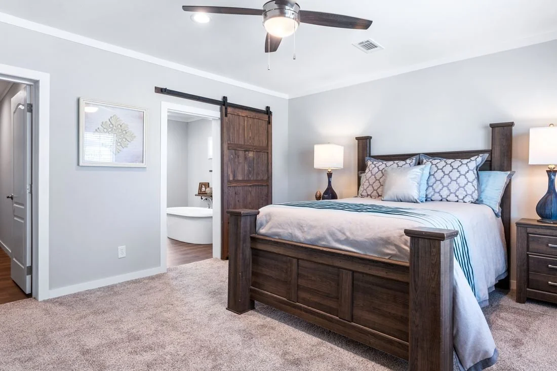 A bedroom with a wooden bed frame, bedside lamps, and a door leading to a bathroom with a bathtub.