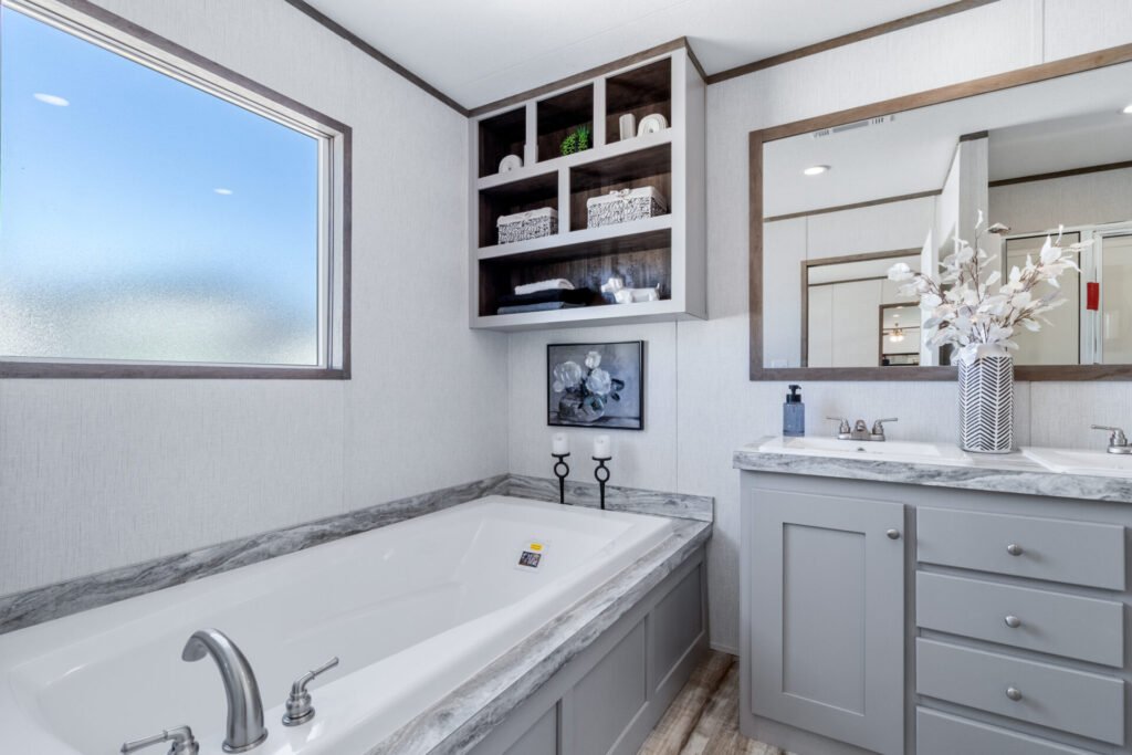 Bathroom with a bathtub, large window, wall-mounted mirror, vanity with a sink, and decorative items including a vase with white flowers.
