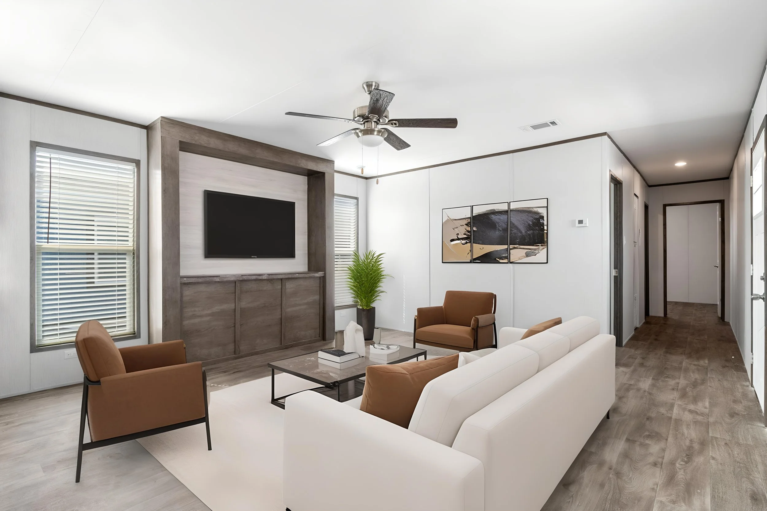 Modern living room with white and brown furniture, a ceiling fan, large wall-mounted TV, abstract art, potted plant, and windows with blinds.