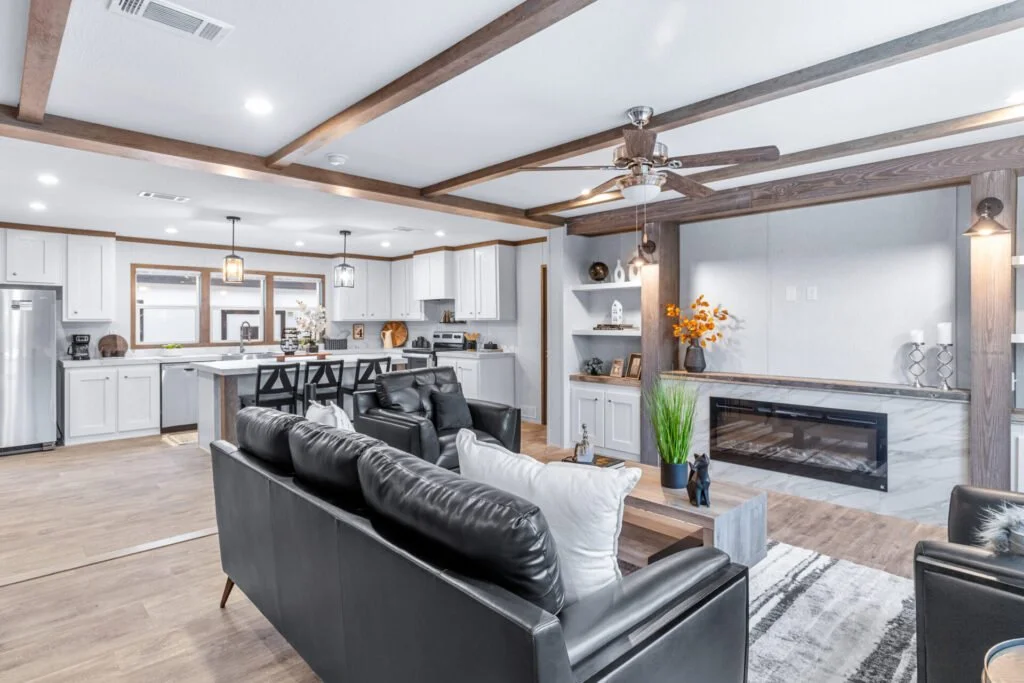 Open-concept living room and kitchen with white cabinets, gray walls, wood accents, black leather sofa, and a fireplace.