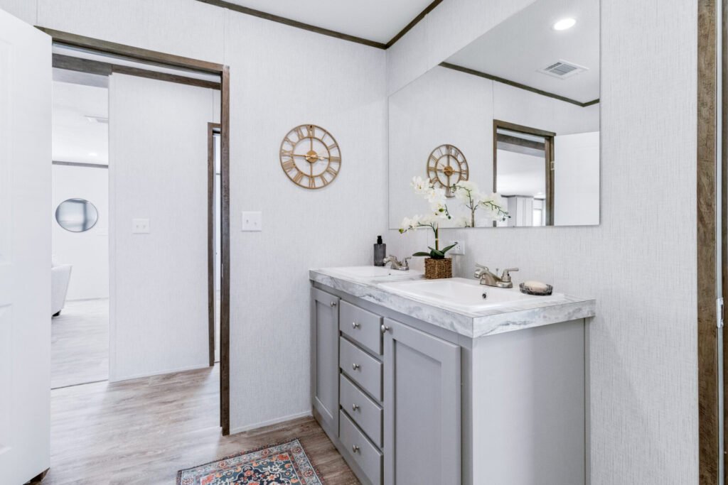 Bathroom with double sink vanity, large mirror, orchid plant, wall clock, and view into an adjacent room.