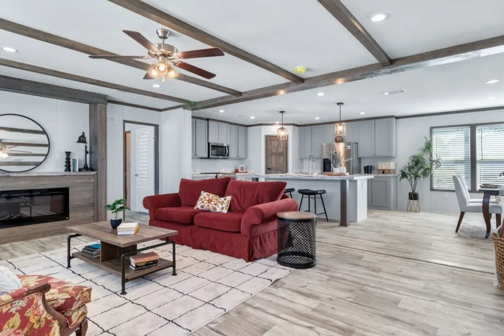 Open-concept living room with a red sofa, coffee table, fireplace, and a kitchen with gray cabinets and an island in a modern home.