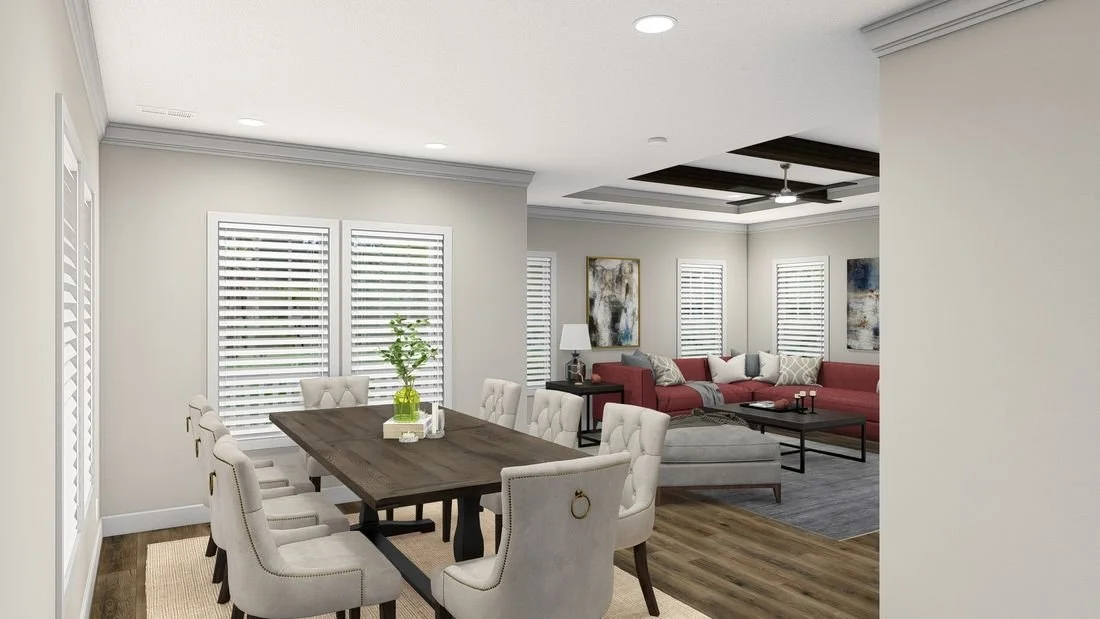 Living and dining room with white walls, hardwood floors, a wooden dining table with eight upholstered chairs, and a sectional sofa with pillows in a neutral and red color scheme.