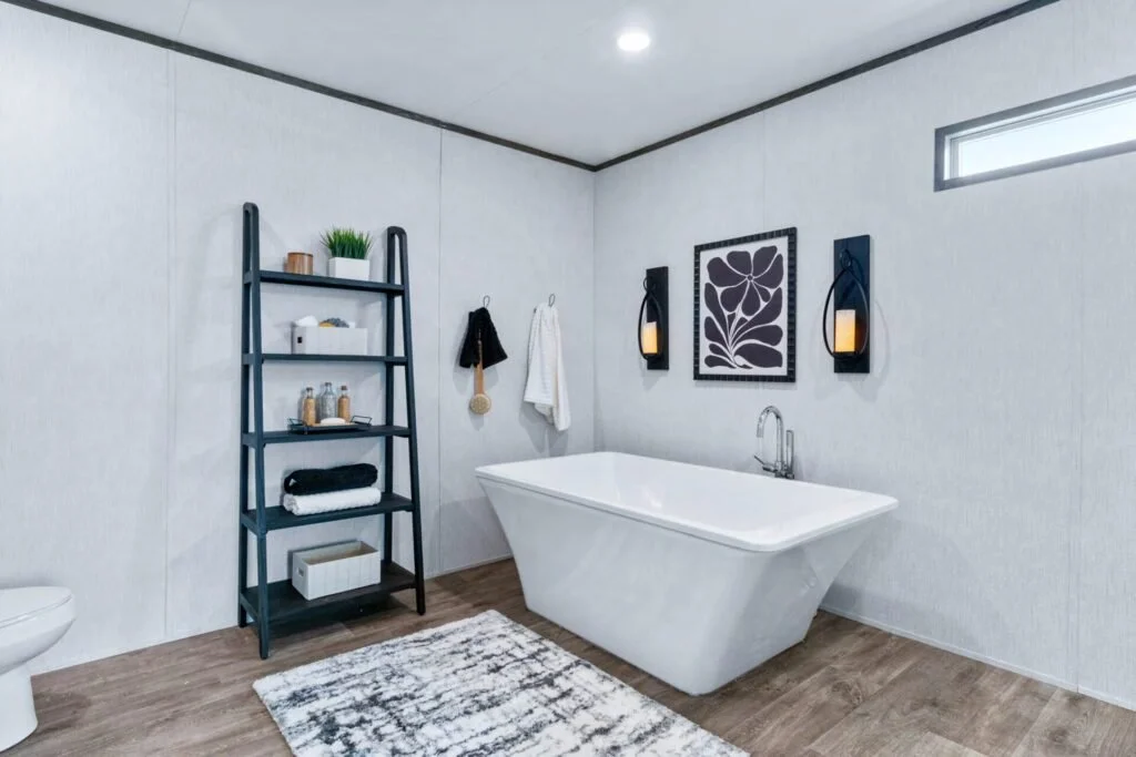 Modern bathroom with a free-standing bathtub, black wall art, candles, a towel rack, and a black ladder-style shelf with decor and towels.