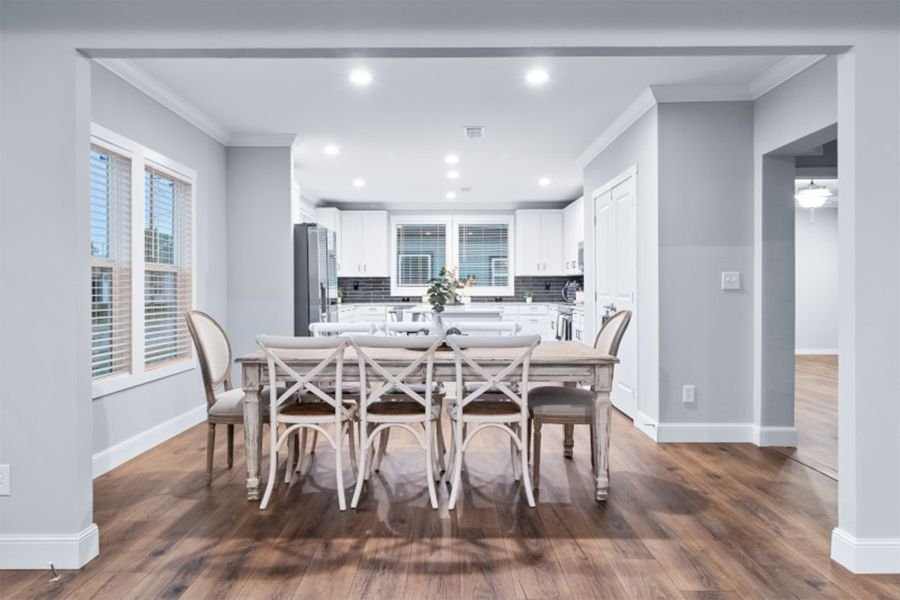Bright open-concept dining area and kitchen with white cabinetry, stainless steel appliances, and wood flooring.