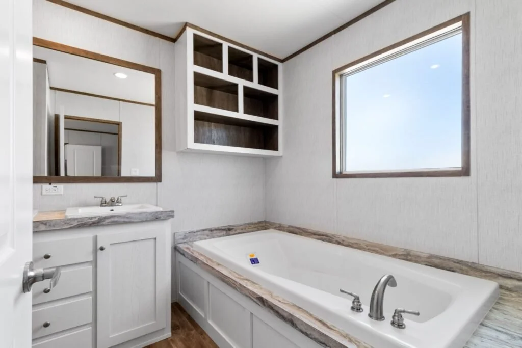 Bathroom with a bathtub, a small vanity with a sink, a mirror, and an open cabinet above the tub, with a large window letting in natural light.