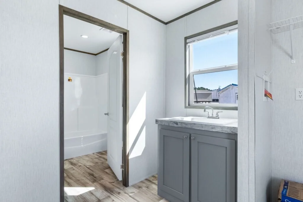 A laundry room with a window, a sink with a gray cabinet, and a small shower area with a door.