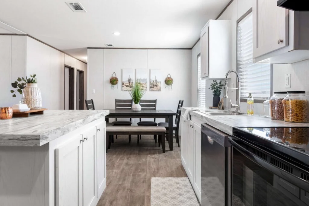Bright kitchen with white cabinets, black appliances, a dining table, and decor including plants and framed artwork.
