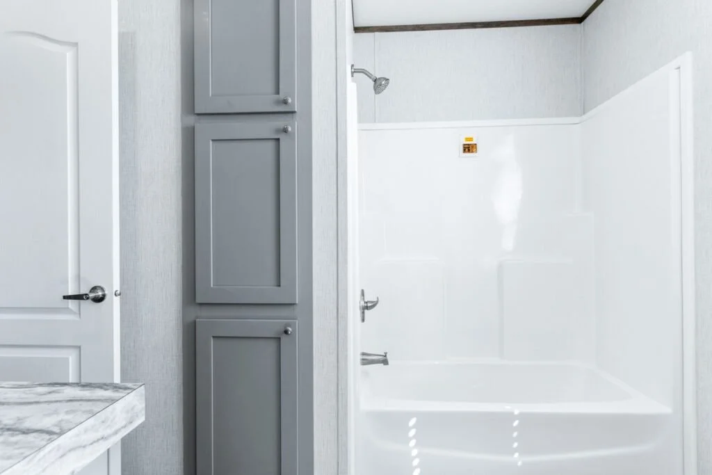 Empty shower with white walls, gray cabinets, and a gray door in a bathroom.