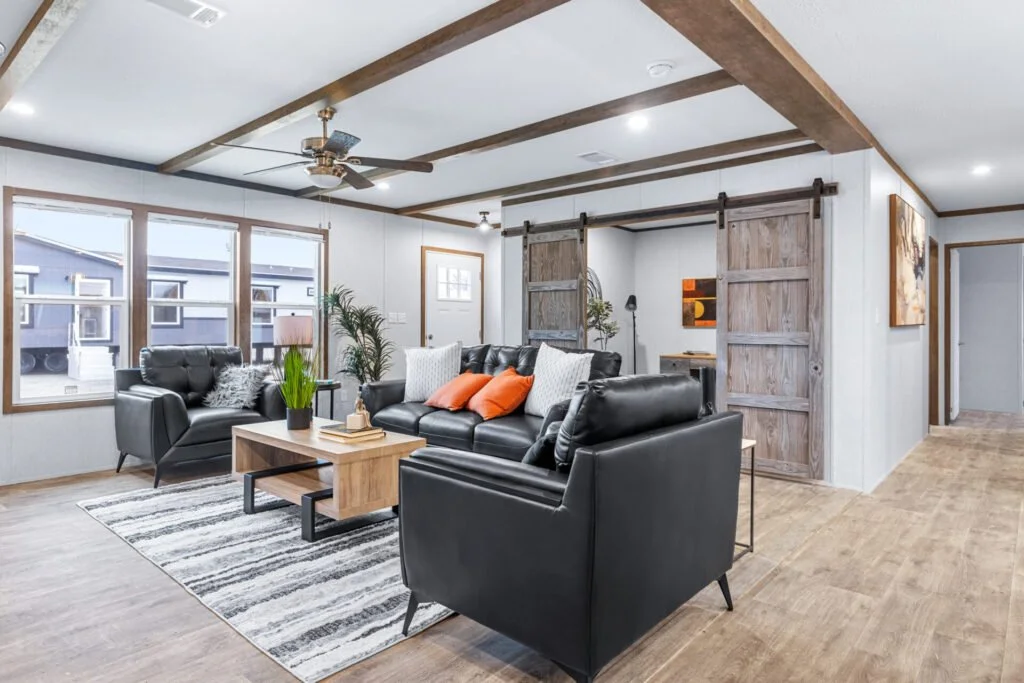 Living room with black leather sofa set, wooden coffee table, striped rug, large windows, sliding barn doors, ceiling fan, and artwork on wall.
