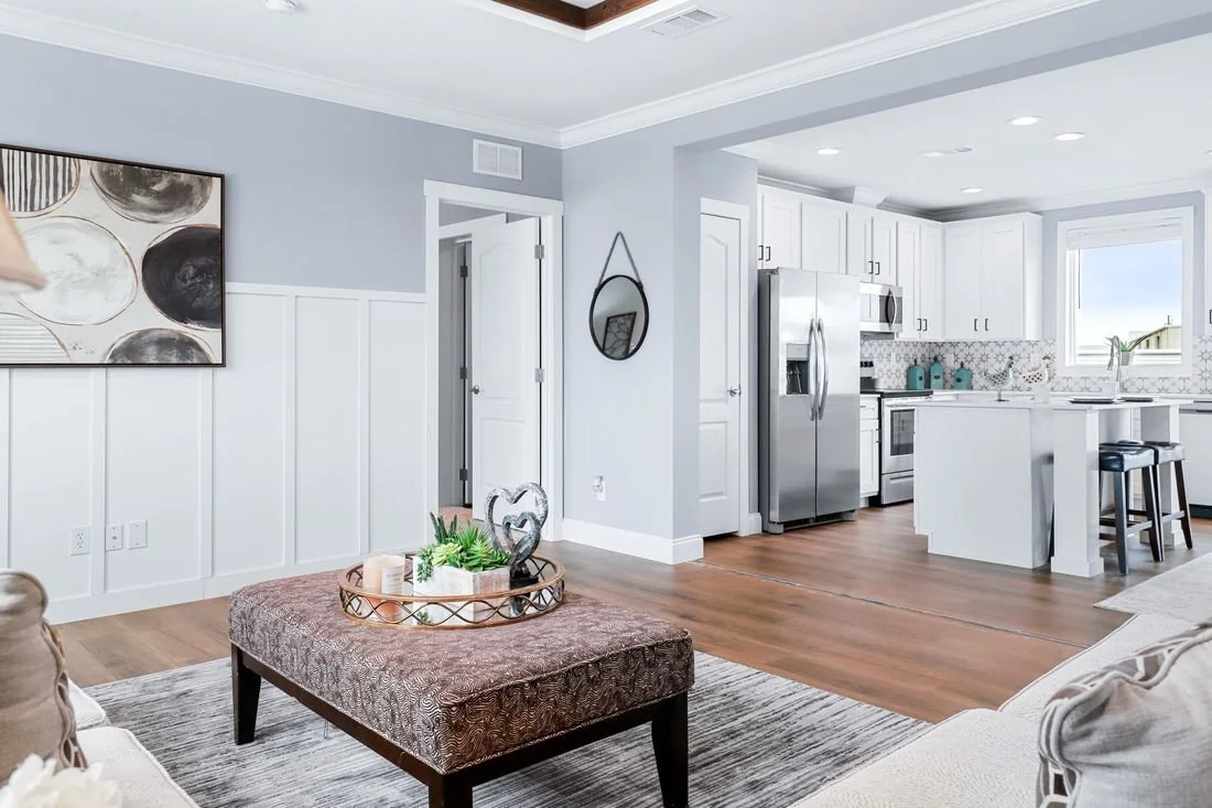 Open-concept living room and kitchen with white cabinets, stainless steel refrigerator, hardwood floors, and modern decor.