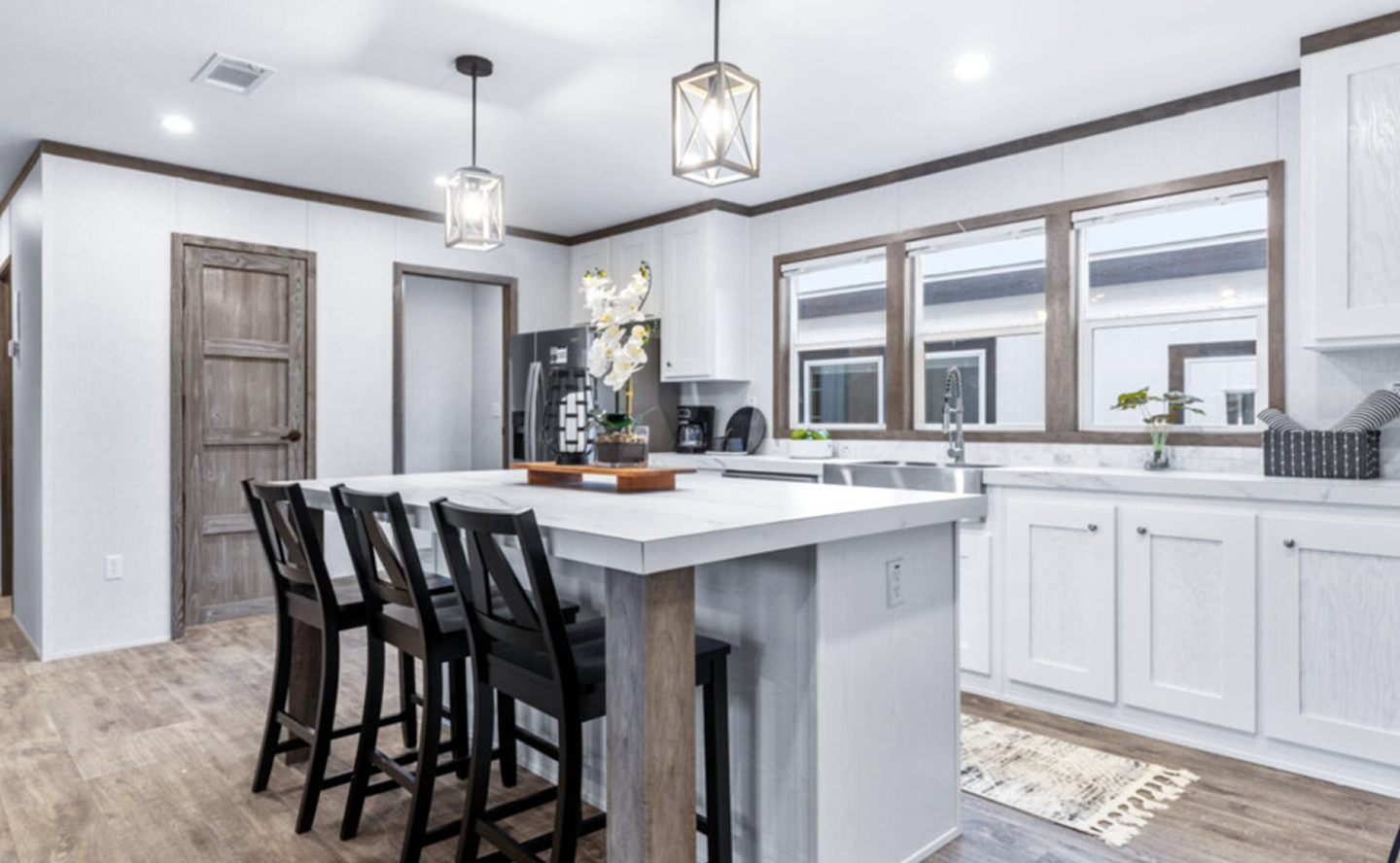 Modern kitchen with white cabinetry, a large island with seating, pendant lighting, and wood accents.