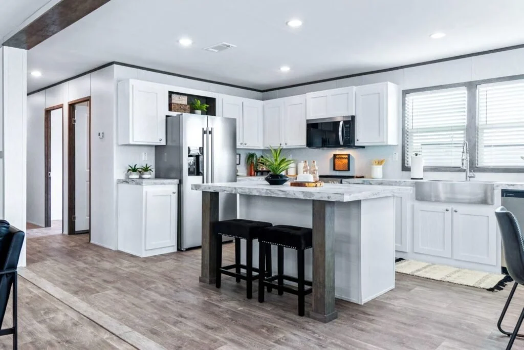 Modern kitchen with white cabinets, stainless steel appliances, a marble countertop island with two black barstools, wooden flooring, and a large window with blinds.