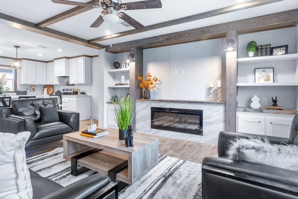Modern living room with black leather sofas, a wooden coffee table, a fireplace, and decorative shelves with ornaments and books.