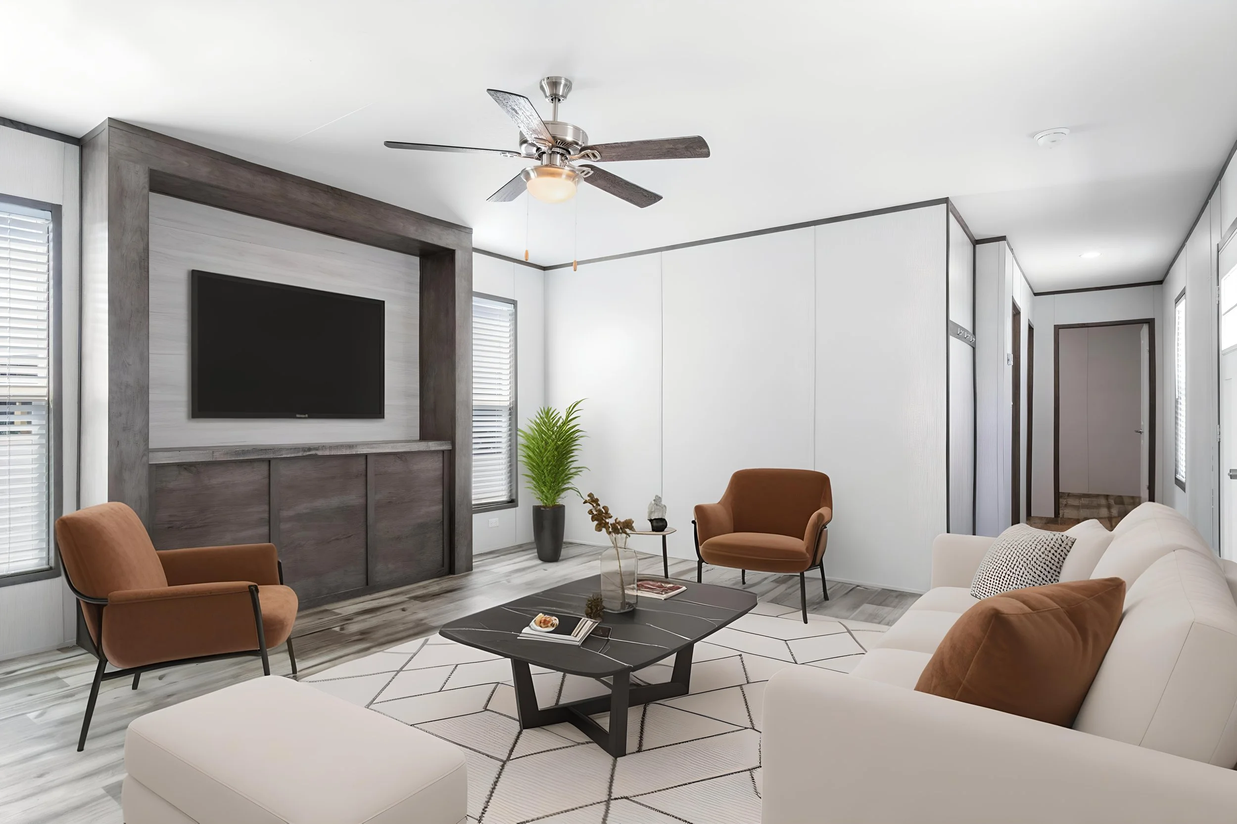 Modern living room with white sofa, brown armchairs, black coffee table, large flat-screen TV, potted plant, and ceiling fan with light fixture.