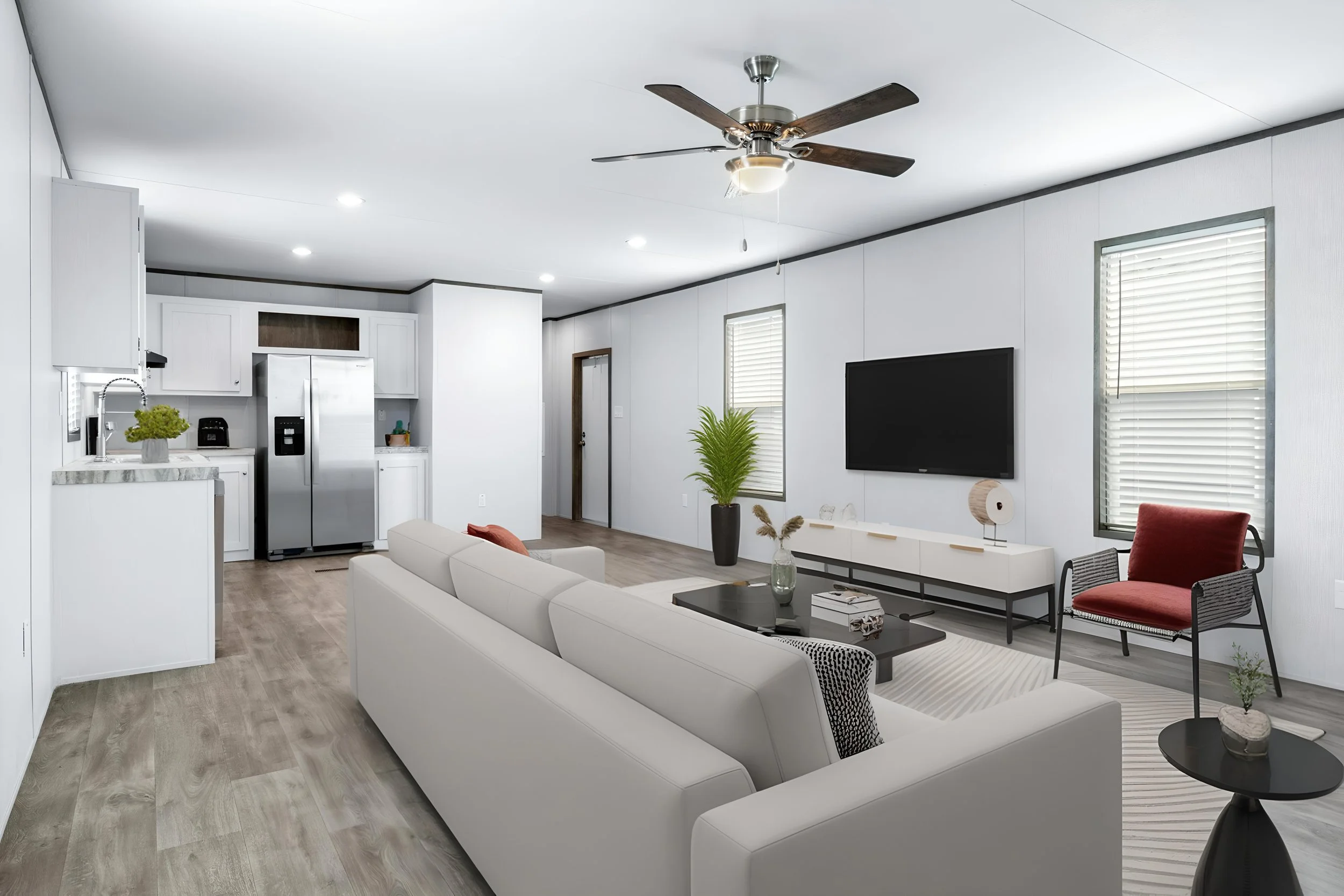 Living room with white sofa, black coffee table, red armchair, large screen TV, potted plants, ceiling fan, and windows with blinds.