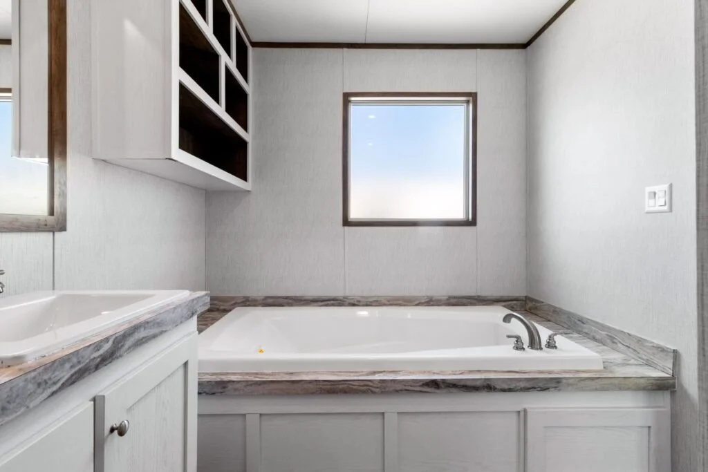 Bathroom with white bathtub, marble countertop, built-in shelves above, window, and light gray walls.