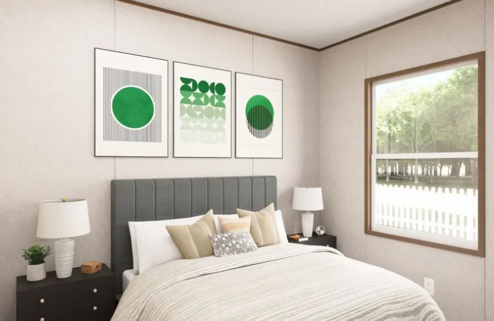 A bedroom with a bed, pillows, two nightstands with lamps, a window showing greenery outside, and three framed abstract art pieces in green and white above the bed.