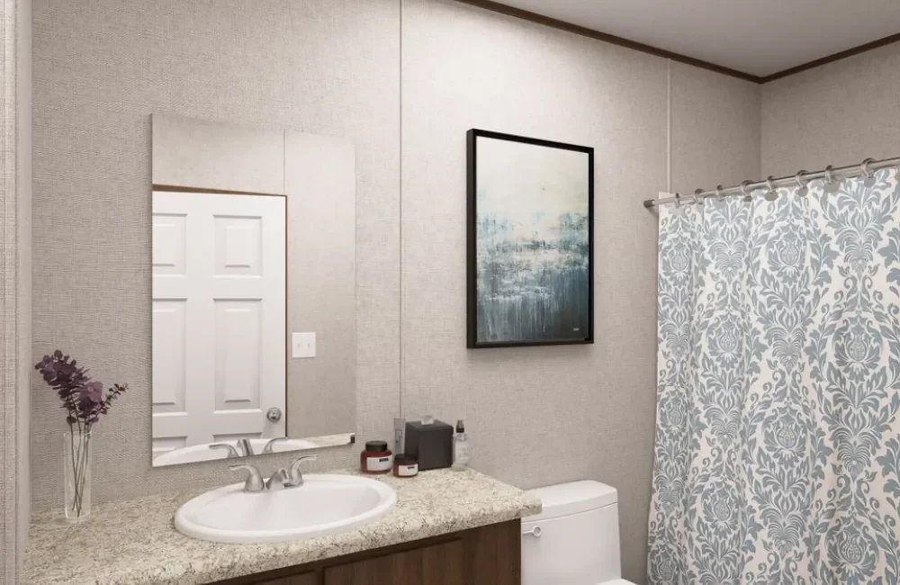 A bathroom with a granite countertop, a white sink, a mirror, some toiletries, a framed abstract painting, a shower curtain with a floral pattern, tiled walls, and a door in the background.