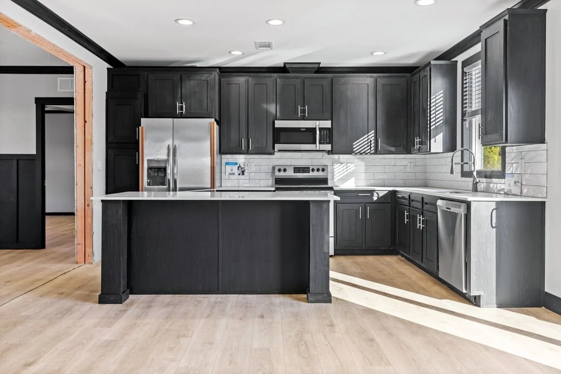 Modern kitchen with dark cabinets, stainless steel appliances, white subway tile backsplash, and light wood flooring.