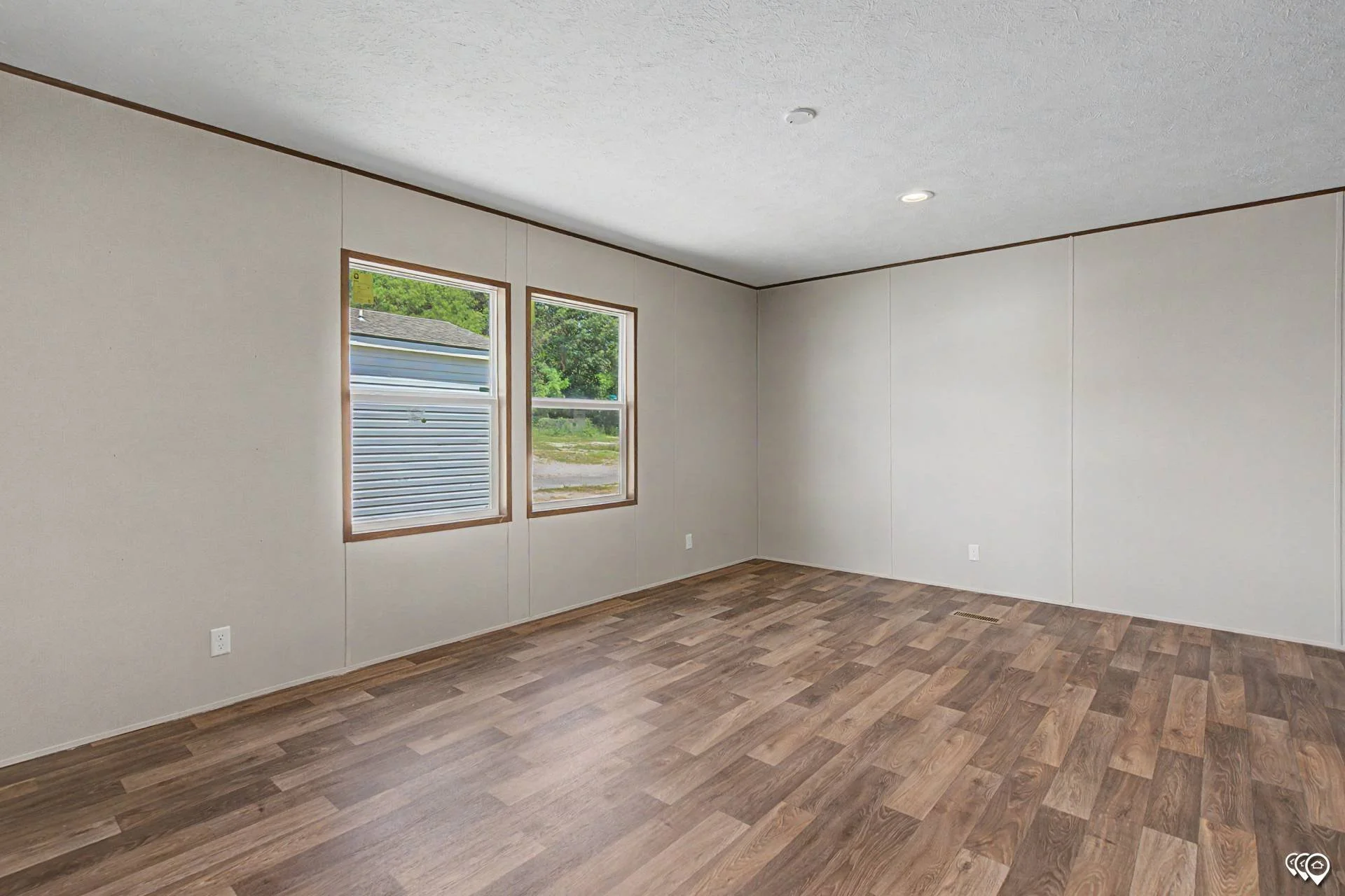 Empty room with white walls, two windows, hardwood flooring, and ceiling lights.
