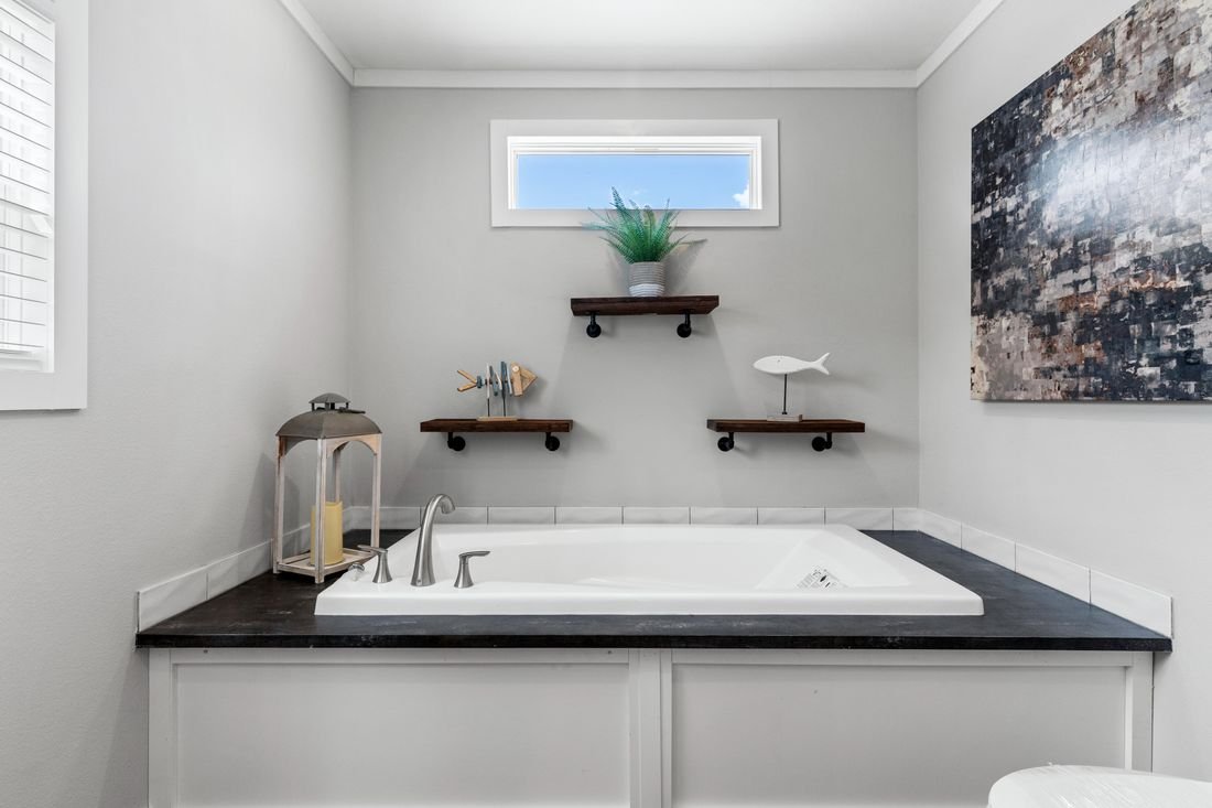Bathroom with a bathtub, wall decor, a small window, a plant, and decorative items including a lantern, a fish sculpture, and a wooden fish on shelves.