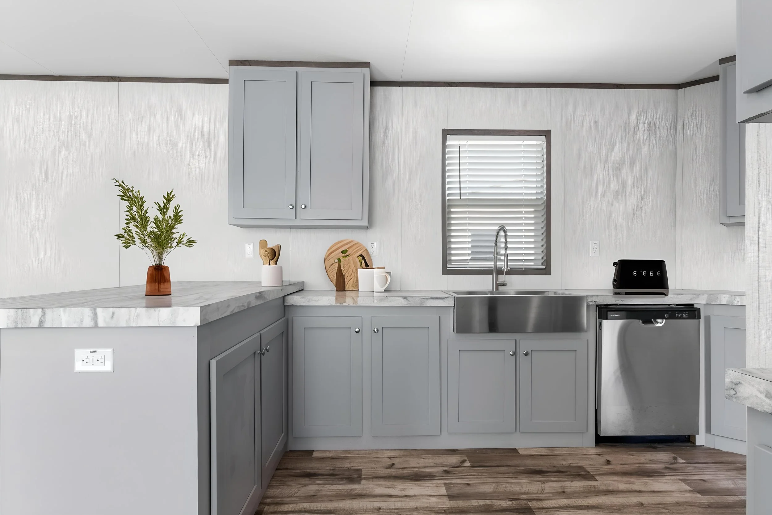 A modern kitchen with gray cabinets, a marble countertop, a stainless steel sink, and a window with blinds.