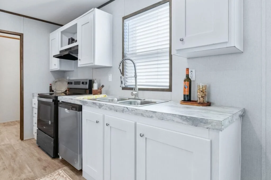 Kitchen with white cabinets, marble countertop, stainless steel sink, and black stove, window with blinds, and decorative items on the counter.