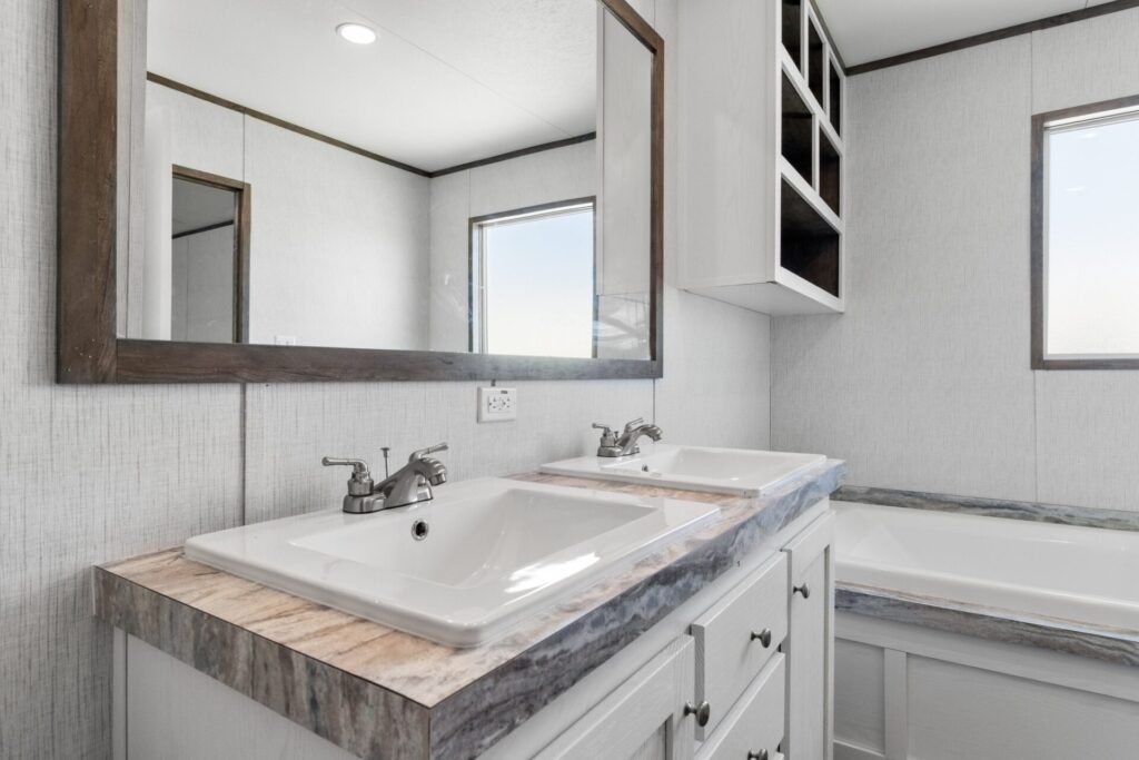 Bathroom with dual sinks, large mirror, and bathtub in a room with white textured walls and gray accents.