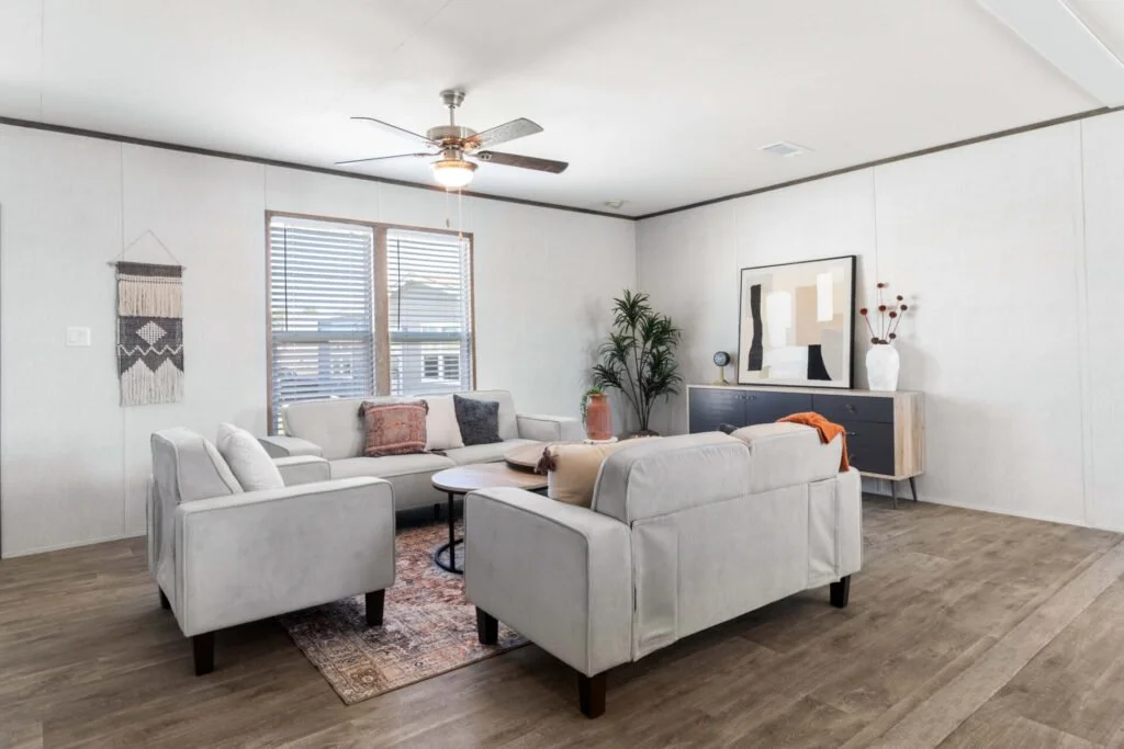Living room with white sofas, a wooden coffee table, a large abstract wall art, a gray cabinet with a vase of flowers, a potted plant, and a window with blinds.