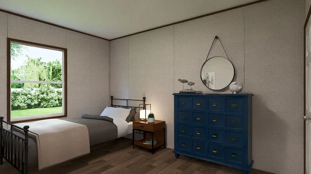 A bedroom with a single bed, a nightstand, a blue dresser, a round mirror, and a window showing green trees outside.