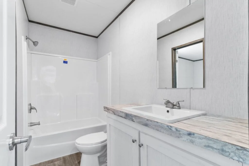 A small bathroom with a bathtub, a toilet, a sink with marble countertop, and a mirror above the sink, all in a neutral color scheme.