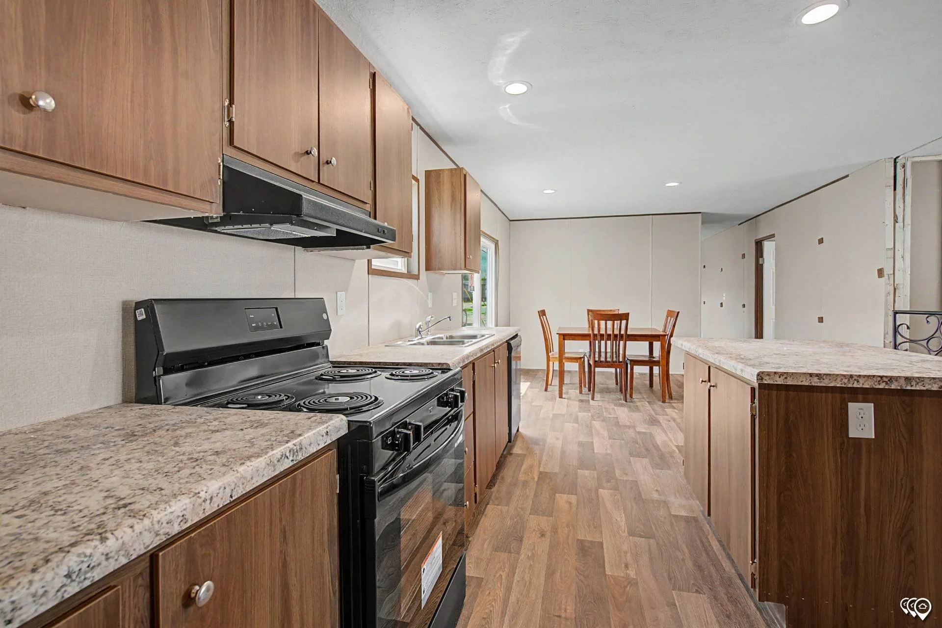 View of a kitchen with wooden cabinets, black stove, granite countertops, a dining table with four chairs, and hardwood flooring.